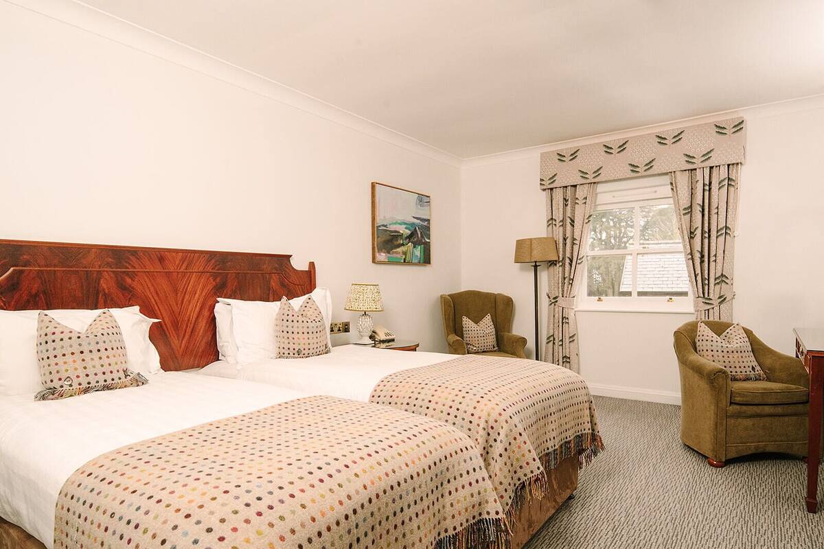 Habitación de hotel con una cama grande, dos mesitas de noche, una silla, una ventana con cortinas y un cuadro en la pared.