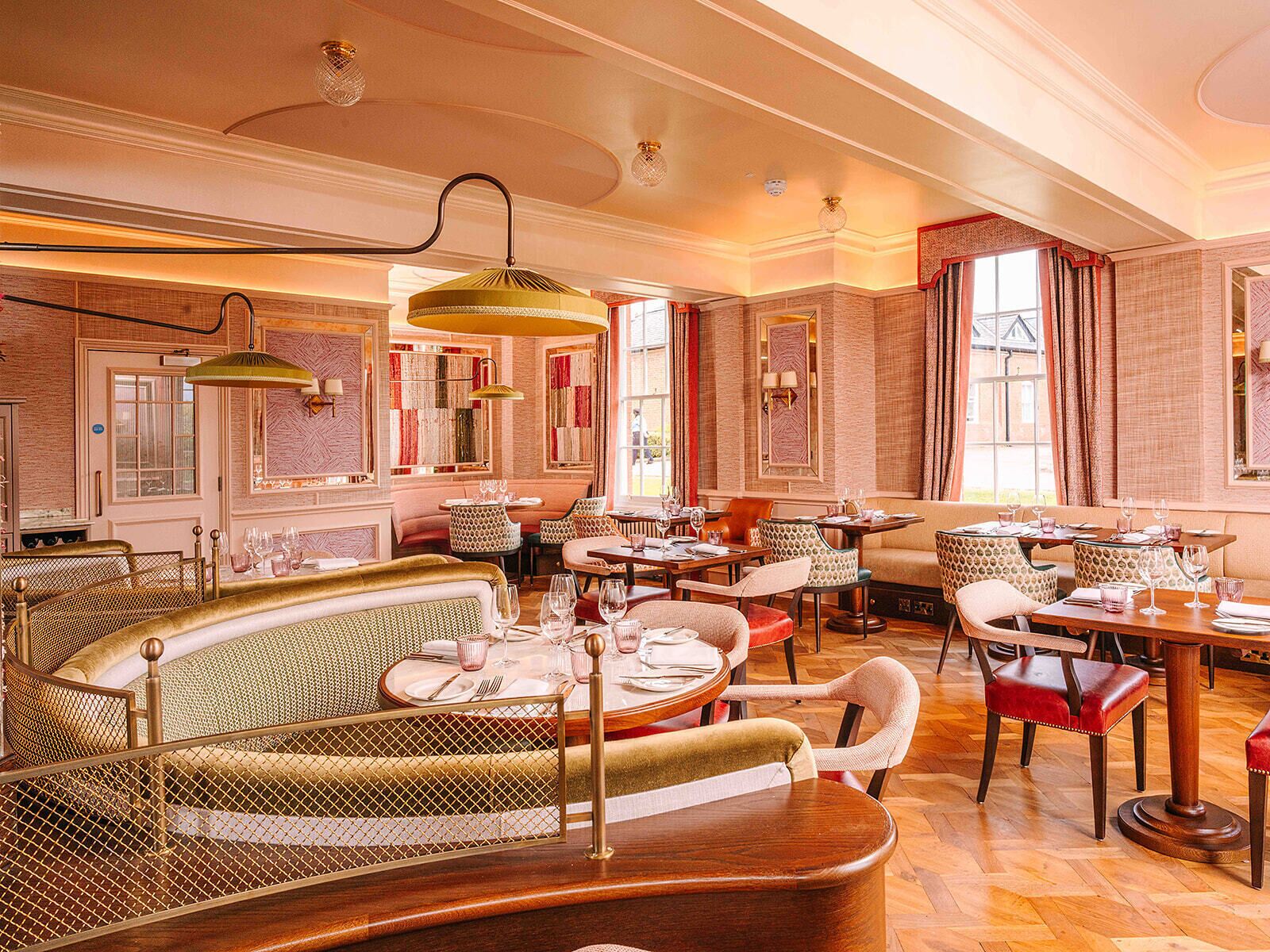Um restaurante com interior clássico, com mobiliário de madeira, paredes estampadas e grandes janelas.