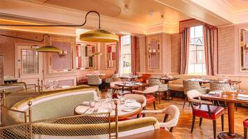 Um restaurante com interior clássico, com mobiliário de madeira, paredes estampadas e grandes janelas.