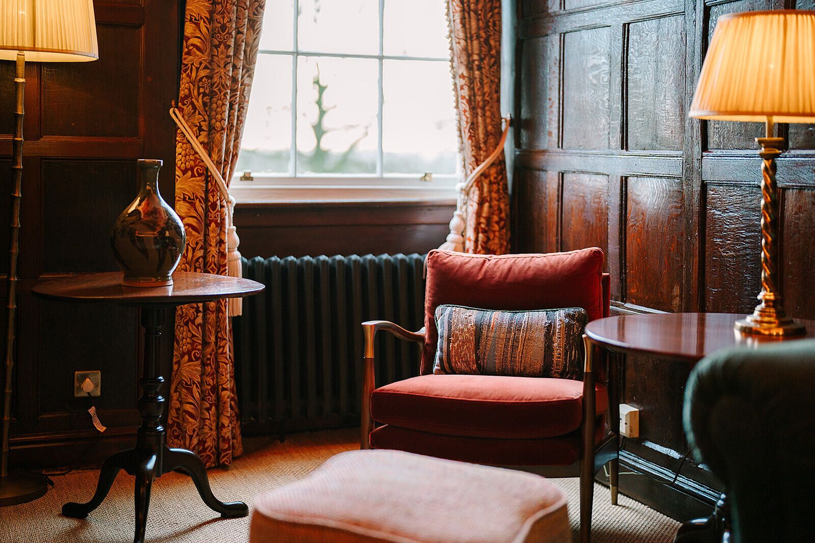 A cozy room with a red armchair, a small table, and a window with curtains.