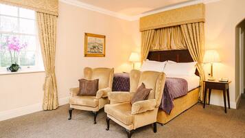 A hotel room with a large bed, two armchairs, a nightstand with a lamp, and a window with curtains.