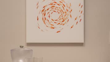 A wall-mounted artwork with a circular pattern, a kitchen counter with a kettle, glasses, and a cabinet below.