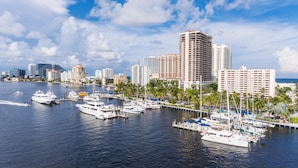 A marina with multiple yachts docked, surrounded by high-rise buildings and palm trees.