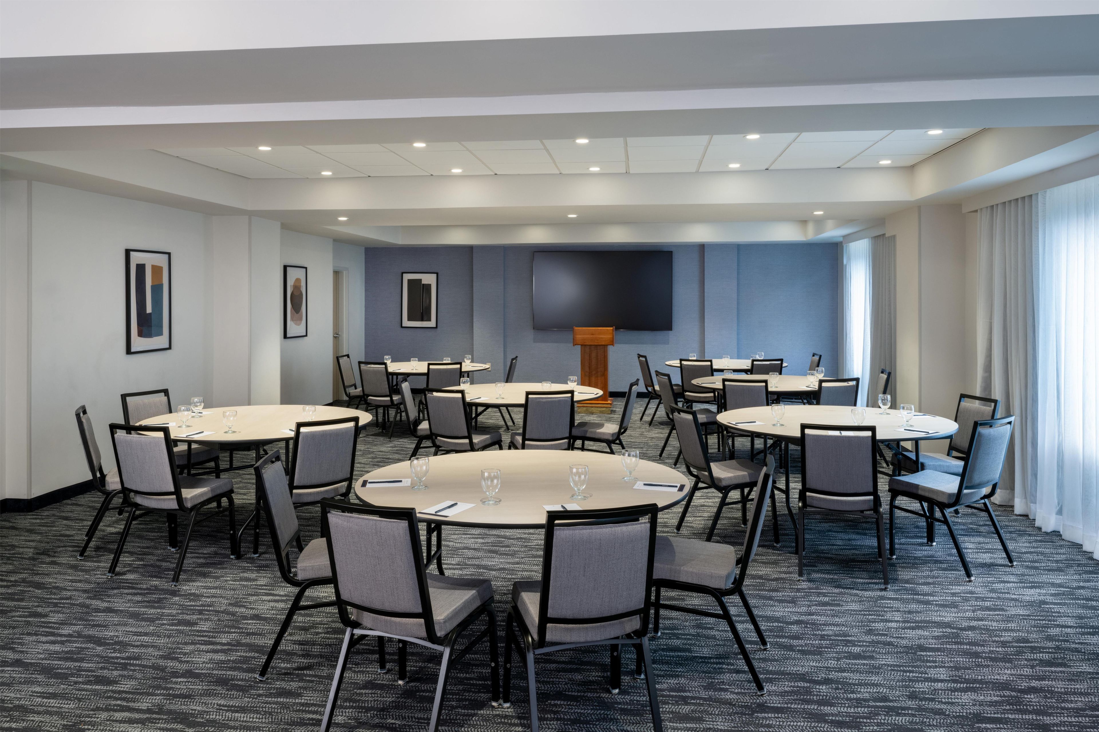Une salle de conférence équipée de plusieurs tables rondes, de chaises et d’un grand écran.