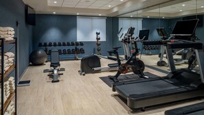 A gym with exercise equipment, a mirrored wall, and a wall of dumbbells.
