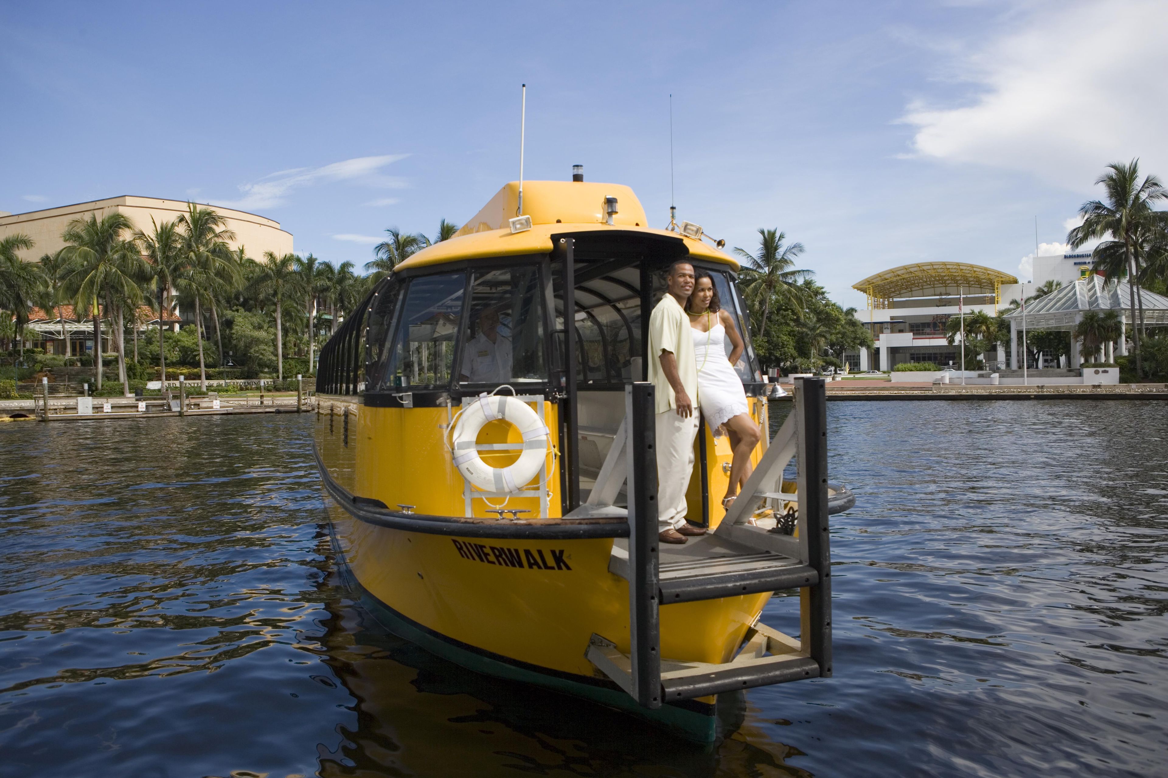 Un bote amarillo con un flotador salvavidas y un hombre y una mujer de pie en la cubierta.