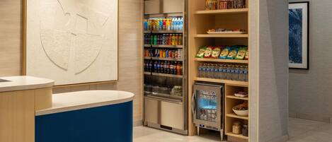 Zona de recepción con mostrador, refrigerador lleno de bebidas y una obra de arte colgada en la pared.