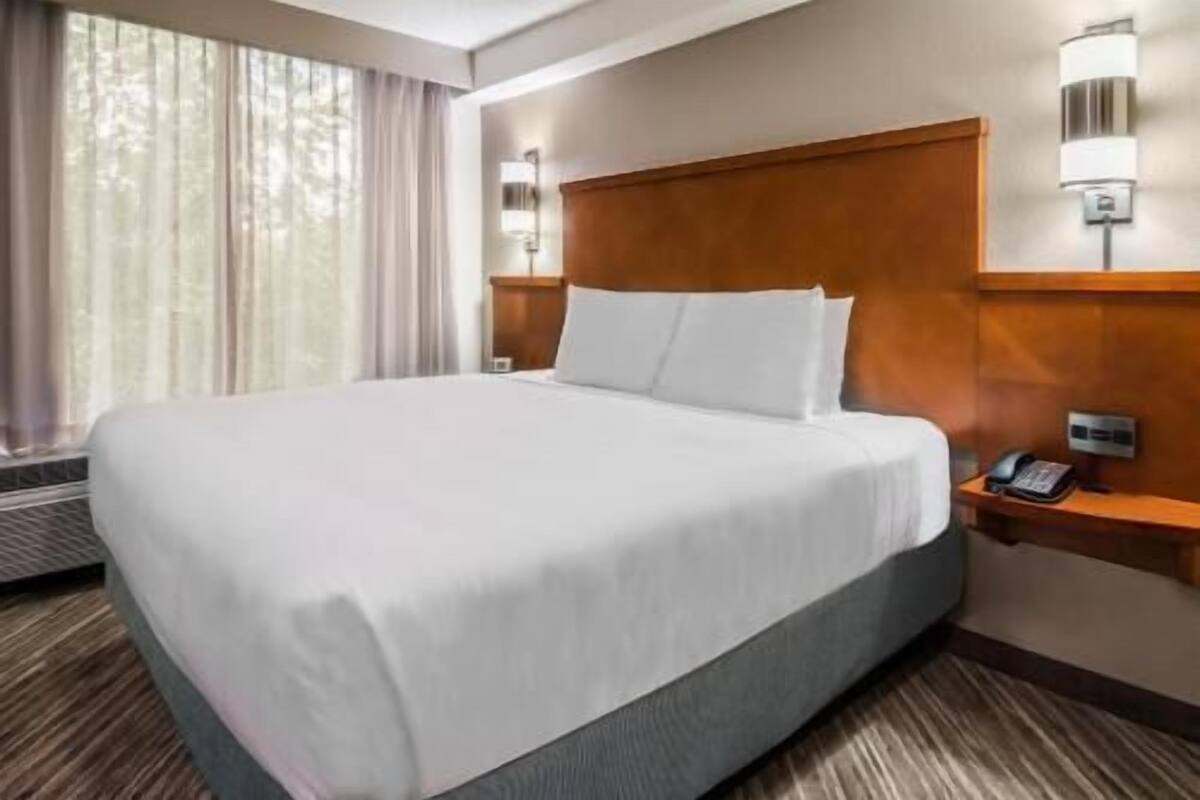 A hotel room with a large bed, a bedside table with a phone, and a wall-mounted lamp.