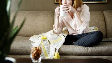 Una persona sentada en un sofá con una manta y una taza.