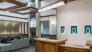 A modern reception area with a wooden reception desk, seating area with sofas, and a large window providing natural light. - Hyatt Place Atlanta/Duluth/Johns Creek (Johns Creek)