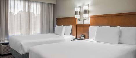 A hotel room with two beds, a large window with curtains, a wall-mounted phone, and a light fixture.