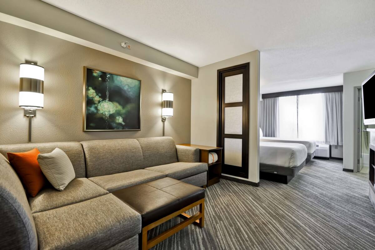 Une chambre d’hôtel avec un canapé, un lit, un tableau au mur et une fenêtre avec des rideaux.