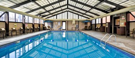 An indoor swimming pool with a high ceiling, clear signage, and a tiled floor.