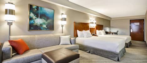 Habitación de hotel con sofá, otoman, dos camas, un cuadro y lámparas fijadas a la pared.