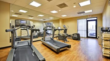 Un gimnasio con cintas de correr, elípticas y un espejo grande.