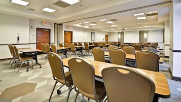 Un salón de conferencias con varias mesas y sillas, equipado con luces de techo y señales de salida.