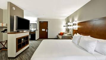 A hotel room with a large bed, a TV, a desk, and a sofa.