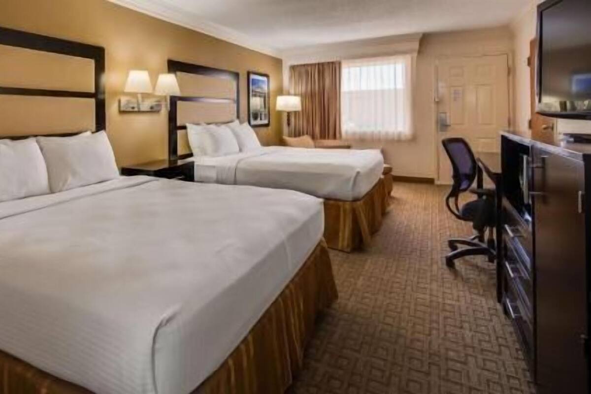 A hotel room with two beds, a desk, a chair, and a television.