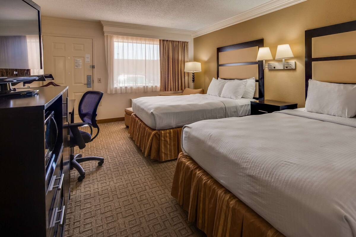 A hotel room with two beds, a desk with a television, and a chair.