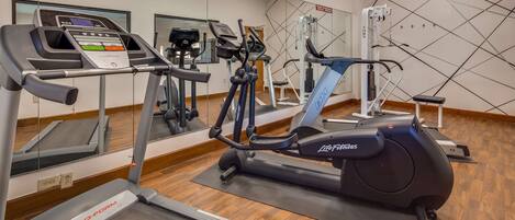 Un gimnasio con diferentes equipos de ejercicio, incluyendo cintas de correr, elípticas y máquinas de pesas.