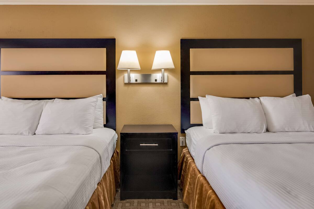 A hotel room with two beds, a nightstand, and a wall-mounted lamp between them.