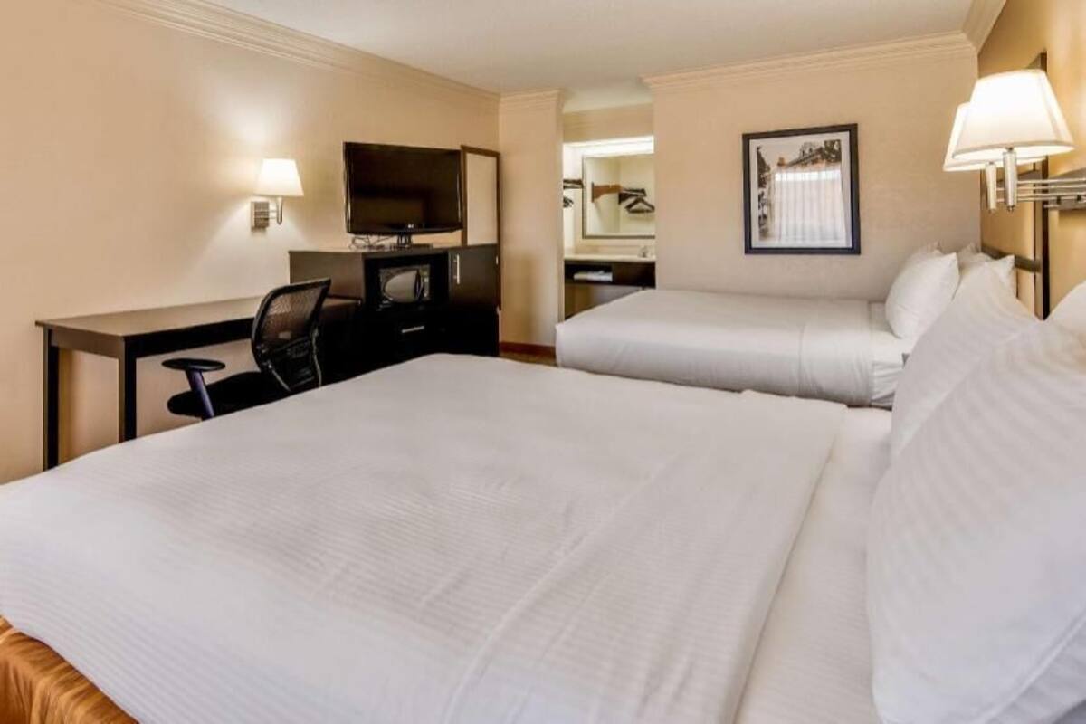 A hotel room with two beds, a desk with a chair, a television, and a mirror.