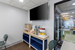 Un área de cocina moderna con un televisor de pantalla plana montado en la pared, una cafetera y un frutero sobre la encimera.