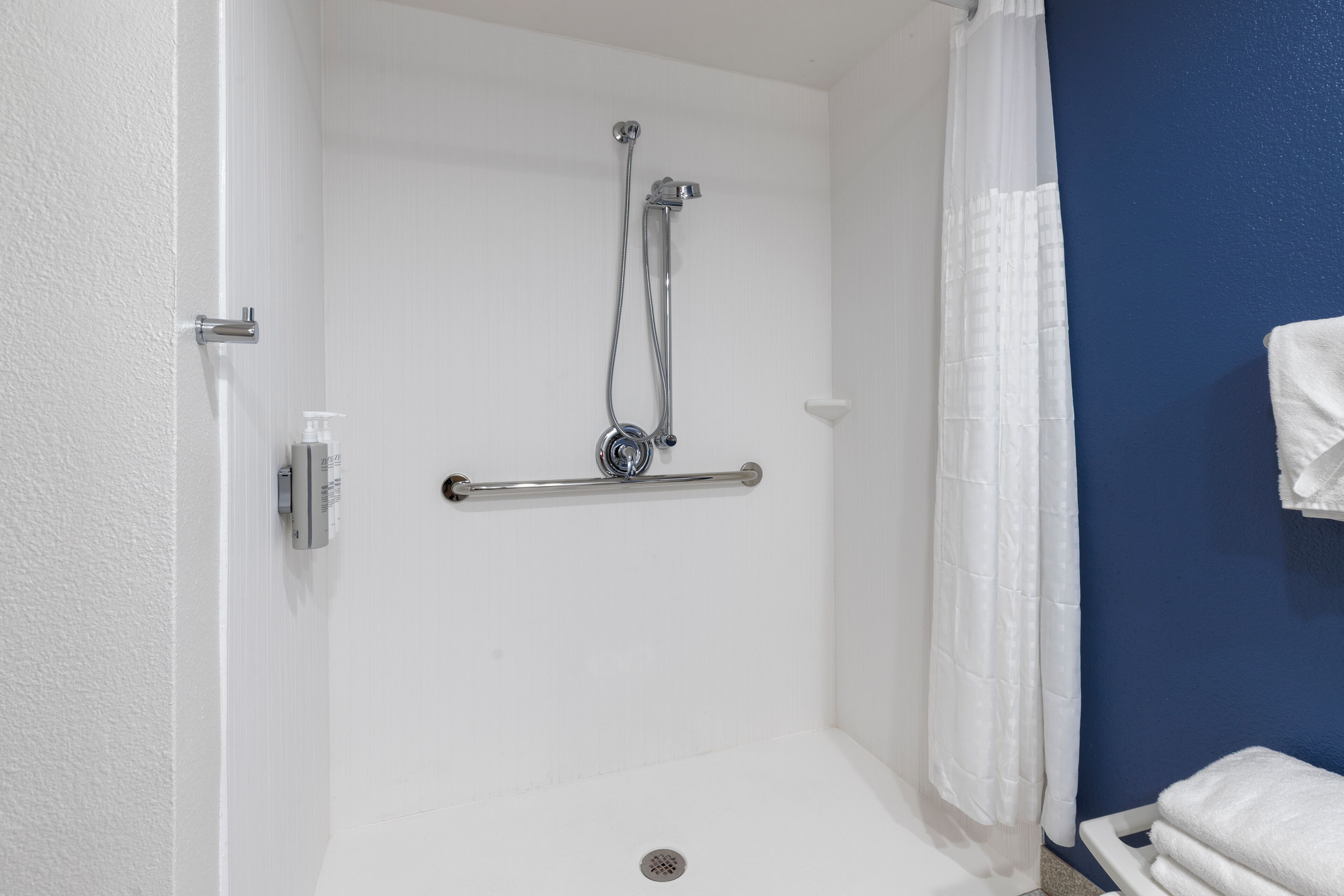 A shower area with a grab bar, a white curtain, and a towel rack.