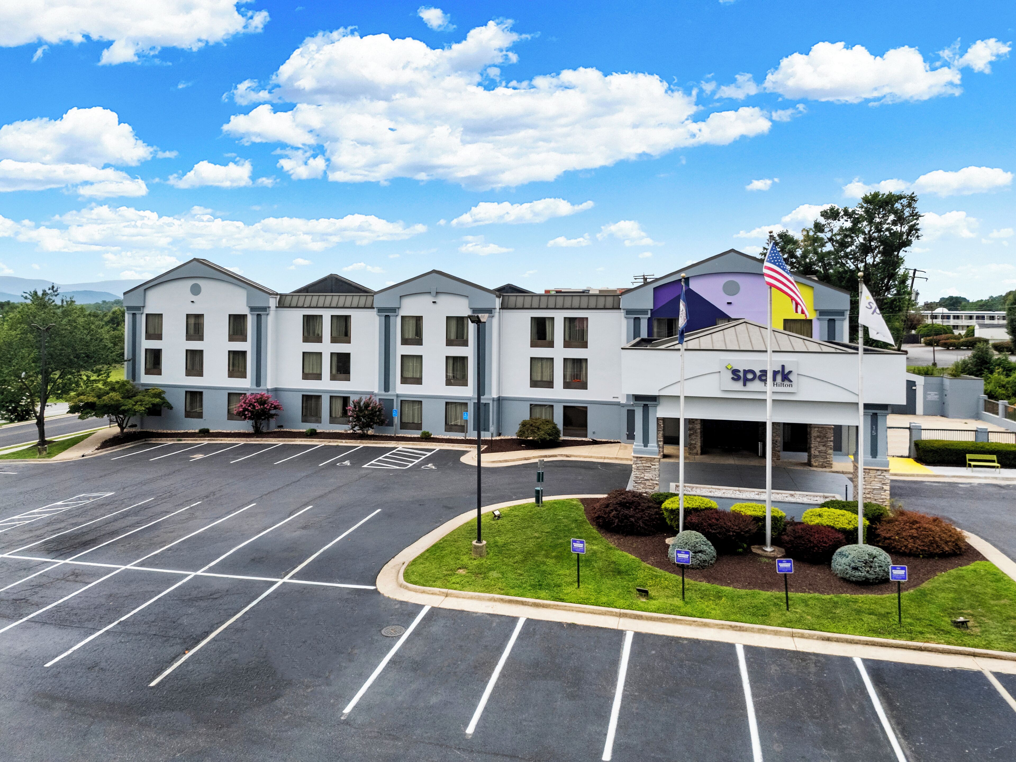 A hotel with a parking lot, a flag, and a signboard.