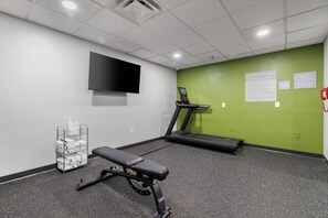A fitness room with a treadmill, exercise bench, and a TV on the wall.