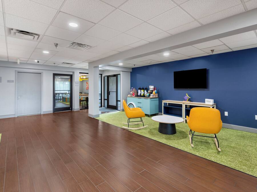 A spacious indoor area with a flat ceiling, a television mounted on the wall, and a seating area with chairs and a small table.