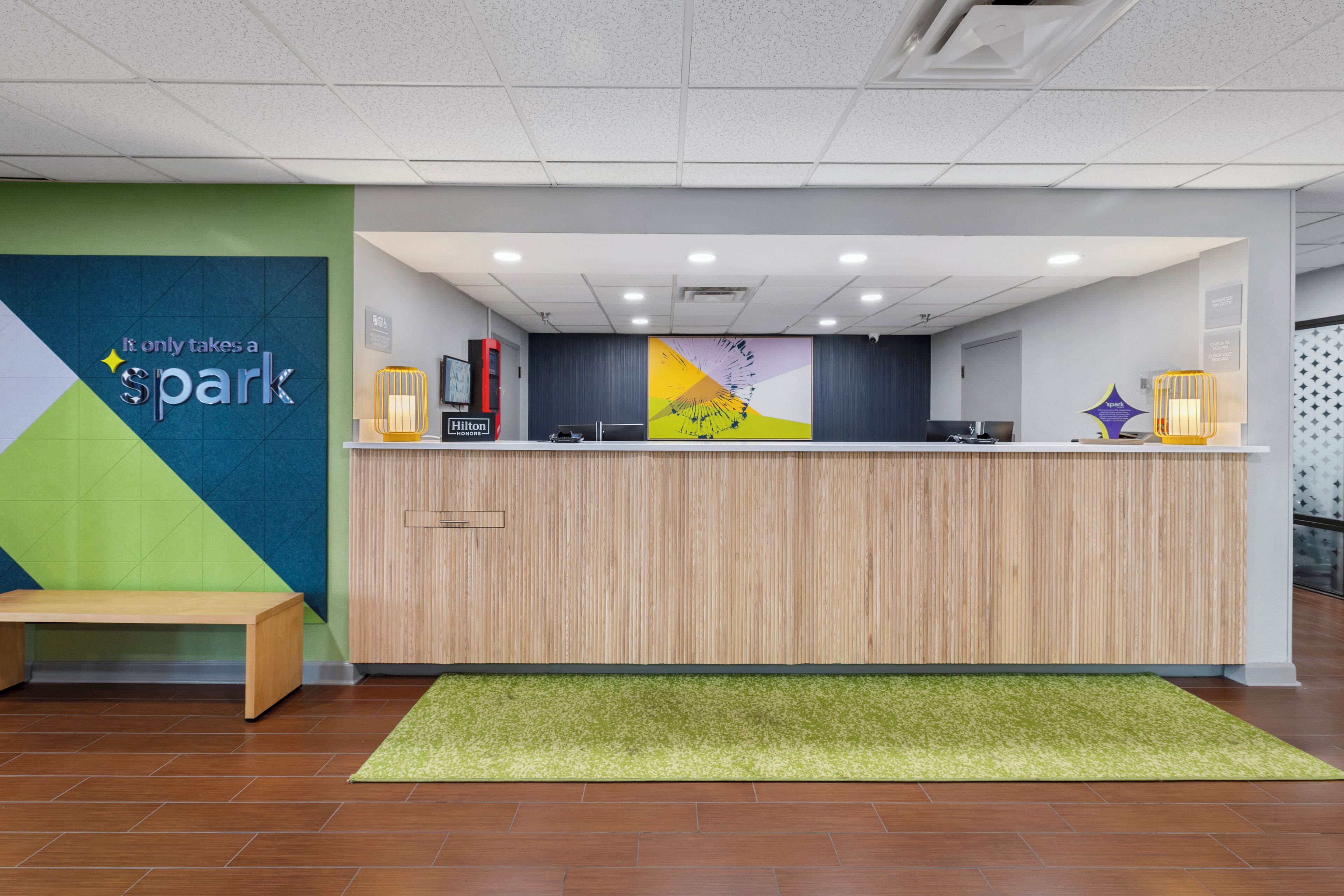 A hotel reception desk with a green and blue wall, a wooden counter, and a green carpet.