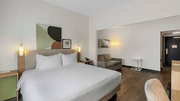 Une chambre d’hôtel avec un grand lit, un bureau, une chaise et un canapé. Des lampes murales et des œuvres d’art ornent les murs.