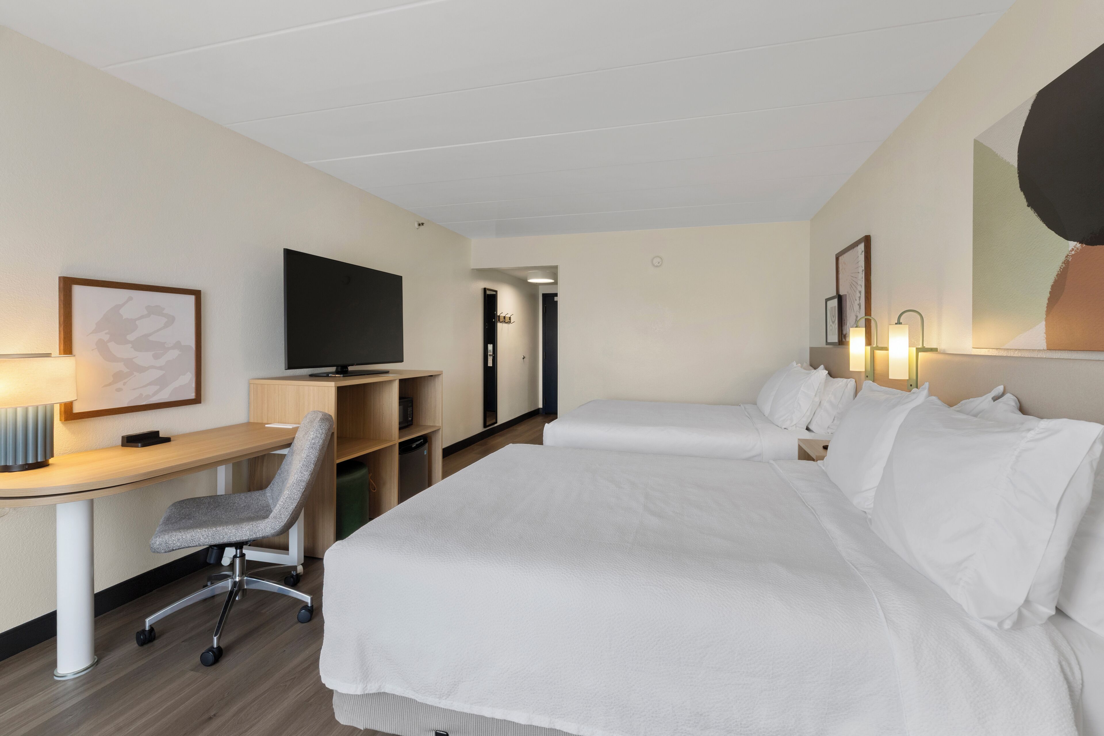 Ein Hotelzimmer mit einem Bett, einem Schreibtisch mit Stuhl, einem Fernseher und einer Badezimmertür.