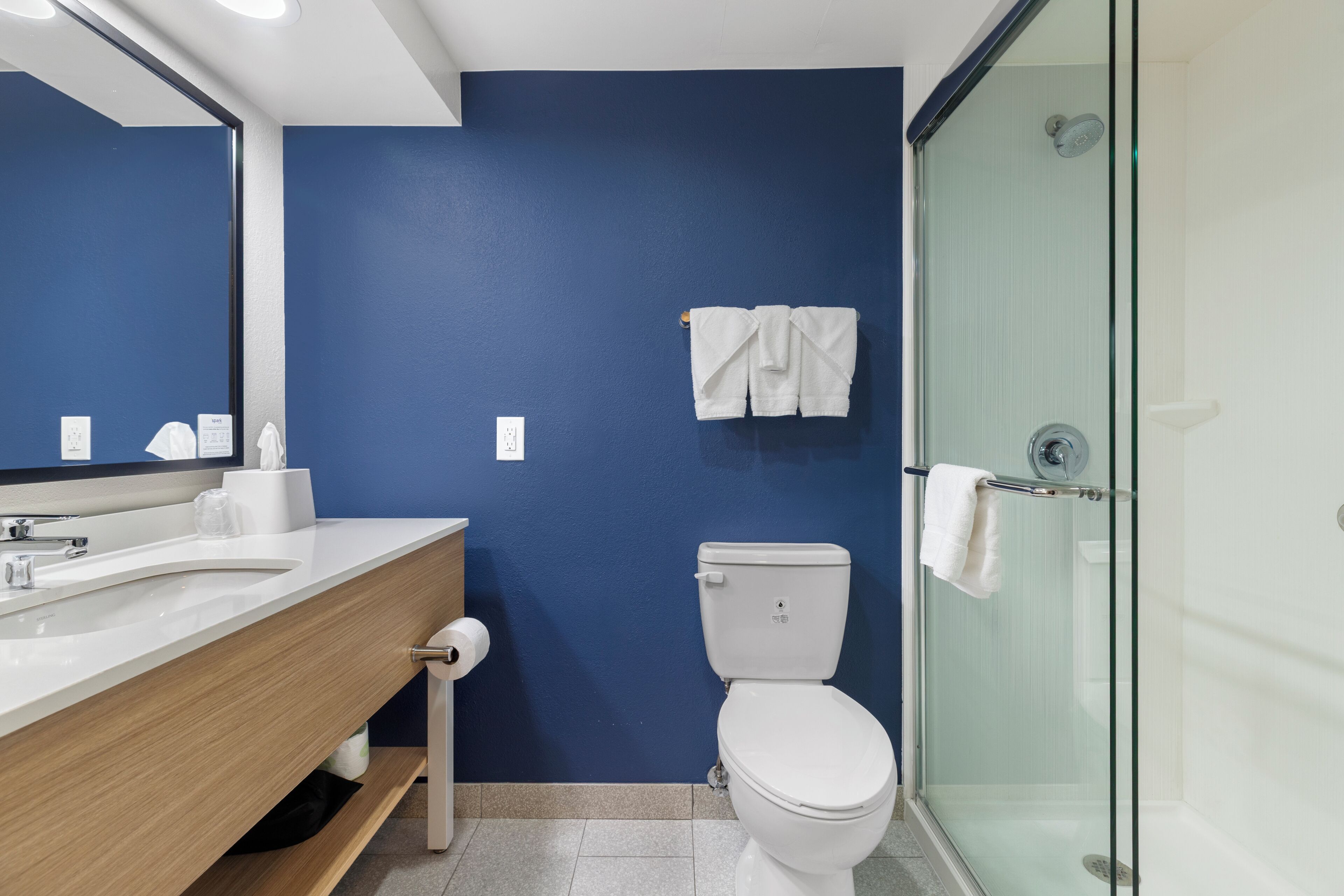A bathroom with a blue wall, a white sink, a toilet, and a glass shower enclosure.