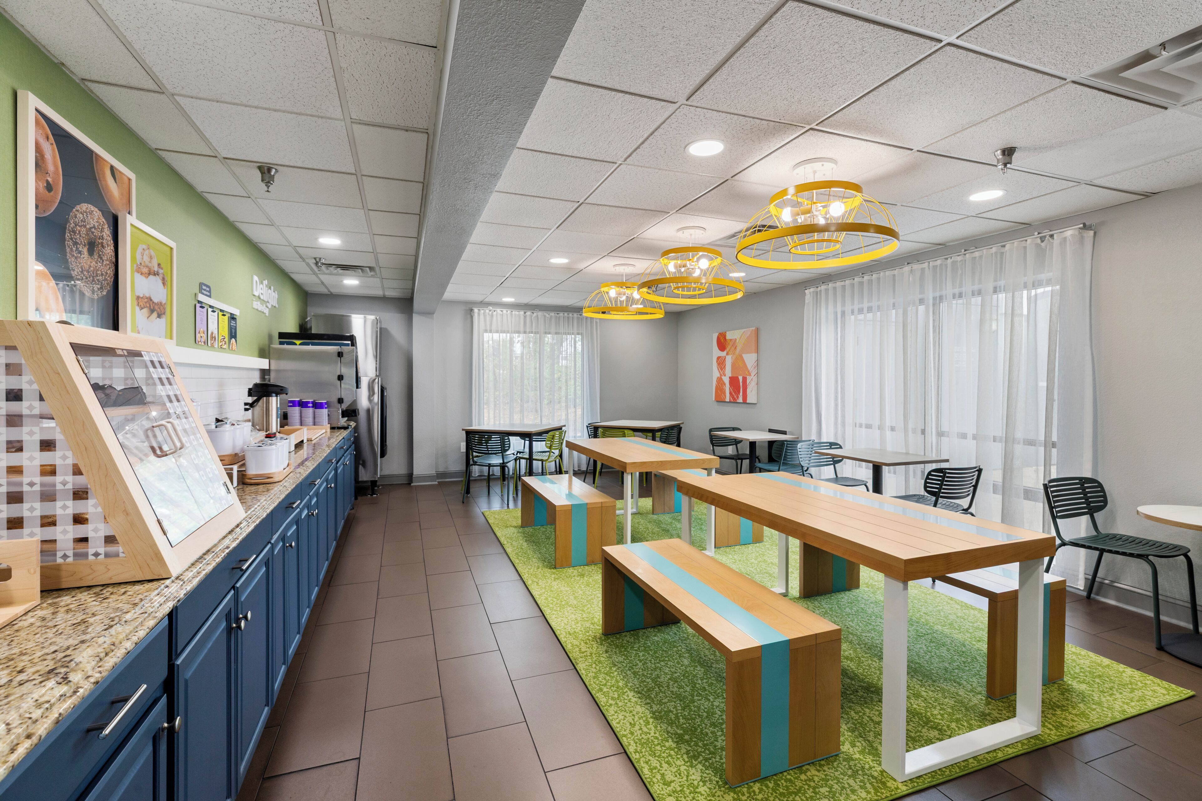 A modern cafe interior with a long counter, seating area with tables and chairs, and a kitchen in the background.