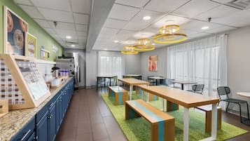 A modern cafe interior with a long counter, seating area with tables and chairs, and a kitchen in the background.