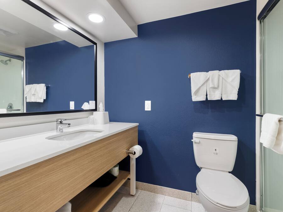 A bathroom with a white sink, a mirror, a toilet, and towels hanging on the wall.