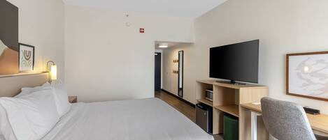 Une chambre d’hôtel équipée d’un lit, d’un bureau, d’une chaise, d’une télévision et d’un four à micro-ondes.