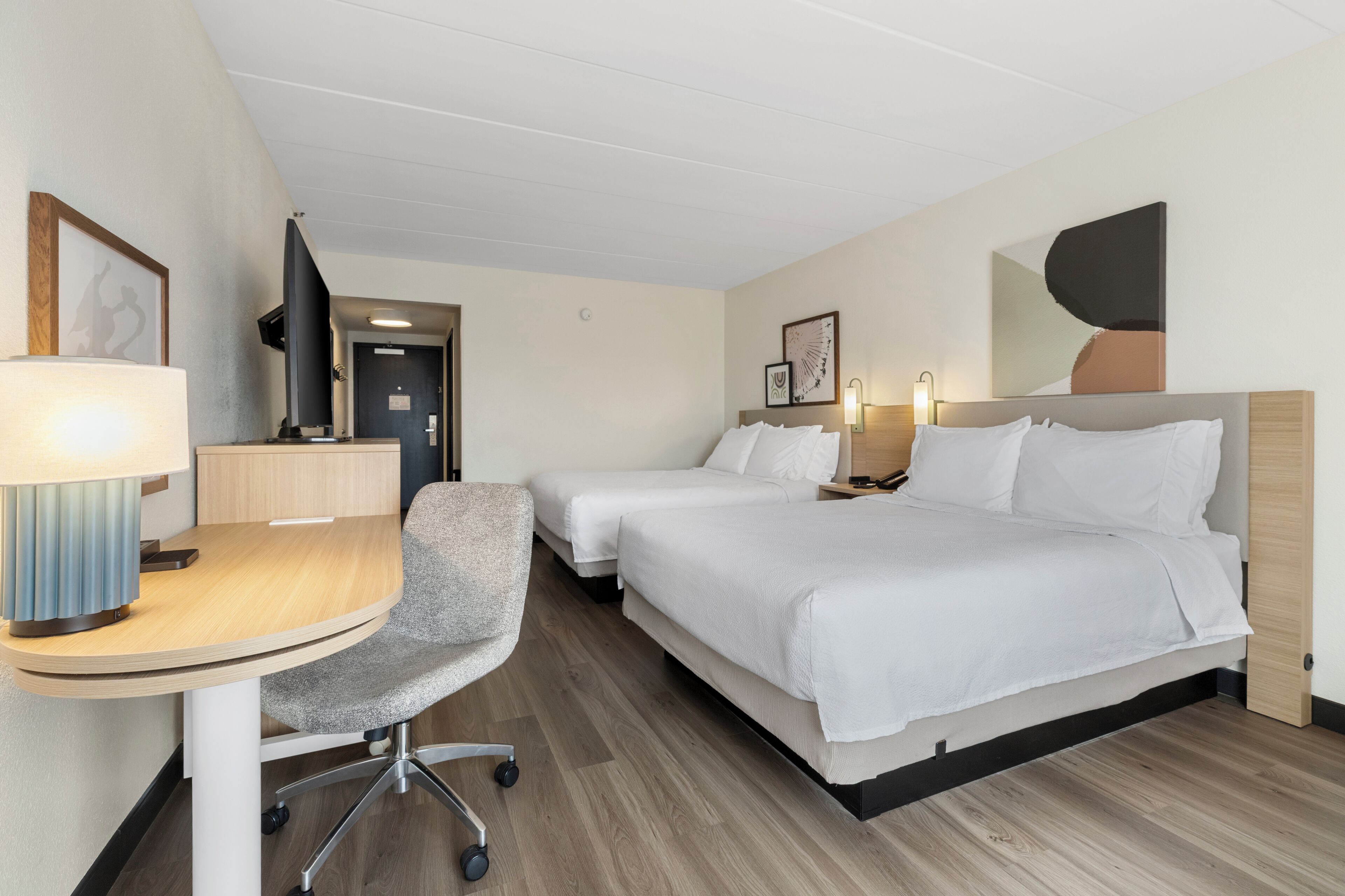 A hotel room with a desk, two beds, a chair, and a television.