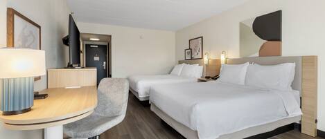 A hotel room with a desk, two beds, a chair, and a television.