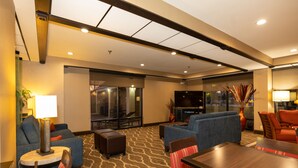 A hotel lobby with a seating area, a flat-screen TV, and a large window.