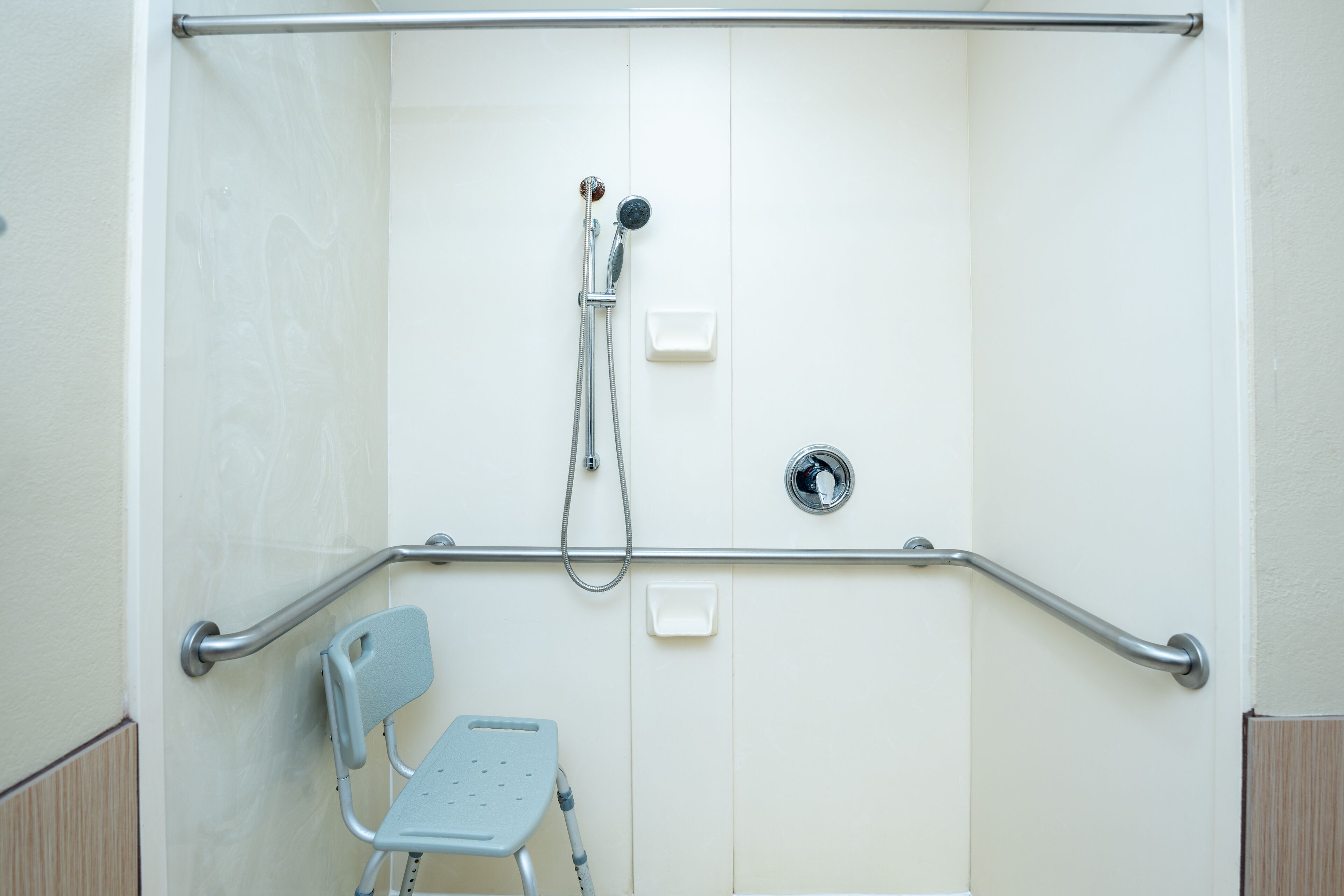 A shower area with a grab bar, a wheelchair-accessible bench, and a handheld showerhead.