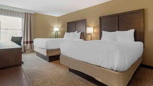 A hotel room with two beds, a desk, and a chair.