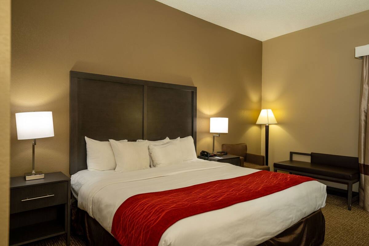 A hotel room with a large bed, two bedside tables, a desk, and two lamps.