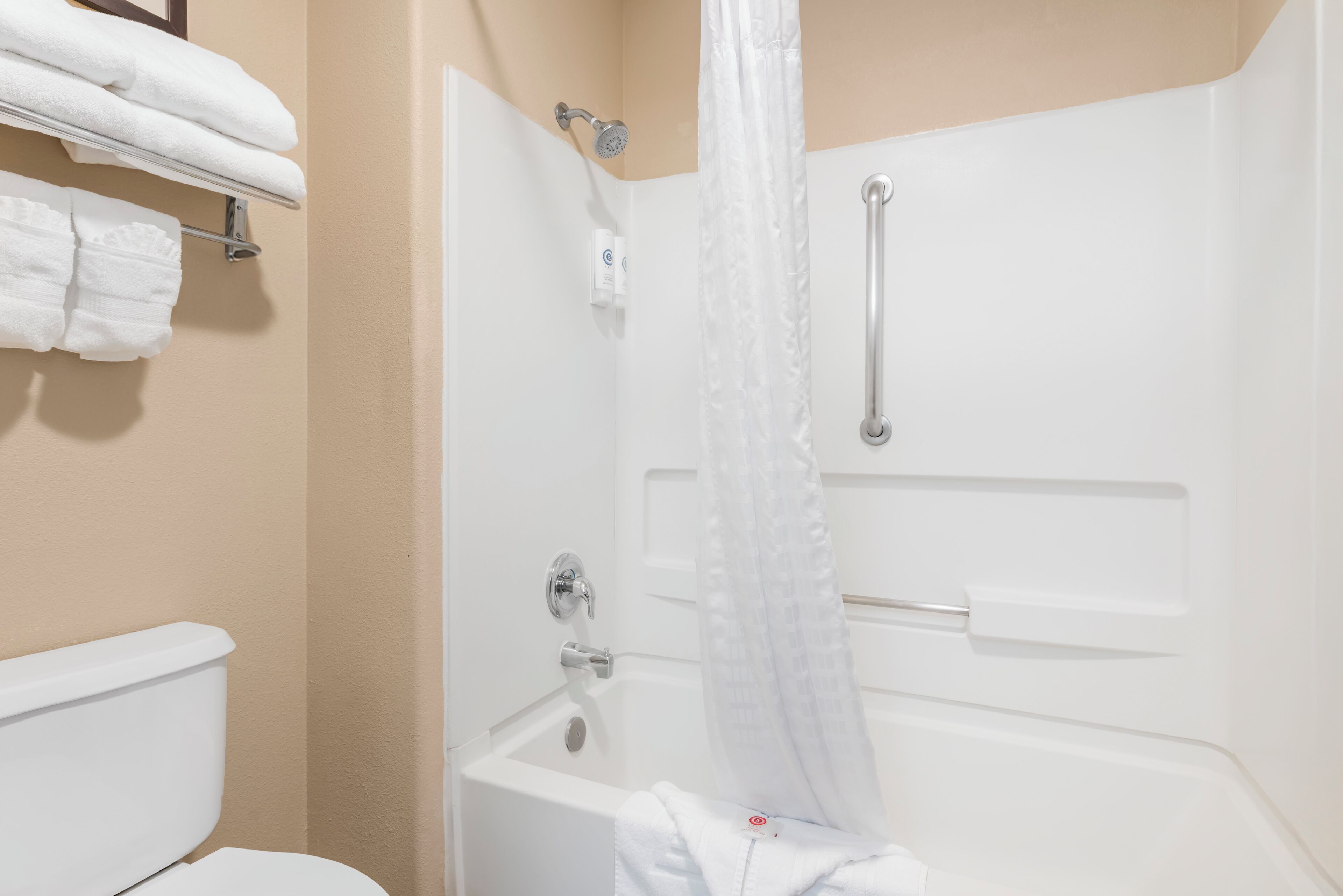 A bathroom with a white bathtub, a shower curtain, a toilet, and a towel rack with folded towels.