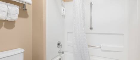 A bathroom with a white bathtub, a shower curtain, a toilet, and a towel rack with folded towels.