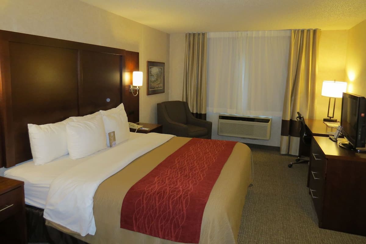 Ein Hotelzimmer mit einem großen Bett, einem Schreibtisch mit Computer, einem Stuhl und einer Klimaanlage.