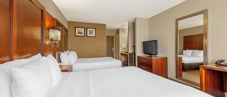 A hotel room with two beds, a desk, a TV, and a large mirror.