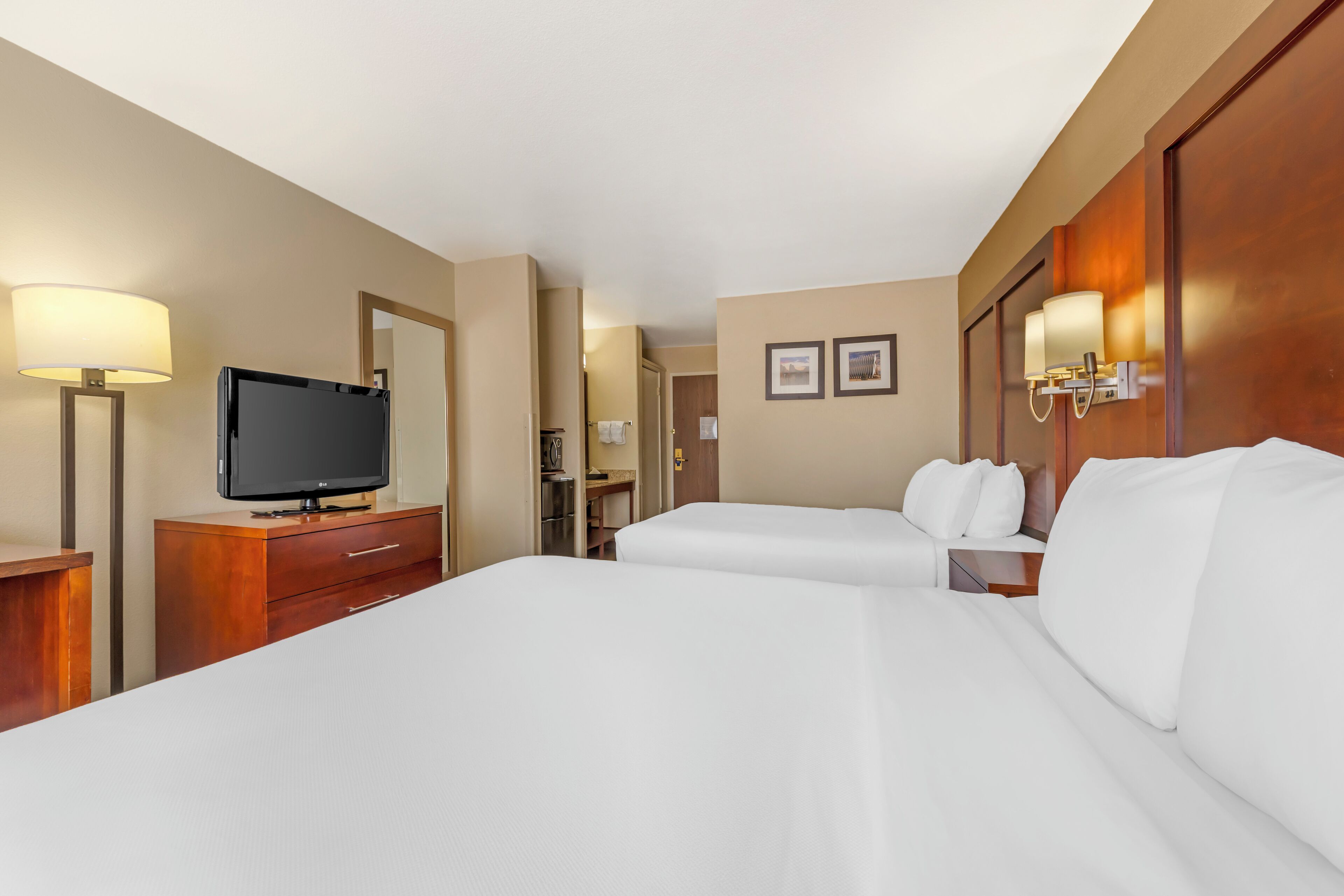 A hotel room with two beds, a TV on a wooden dresser, and a bathroom visible through an open door.